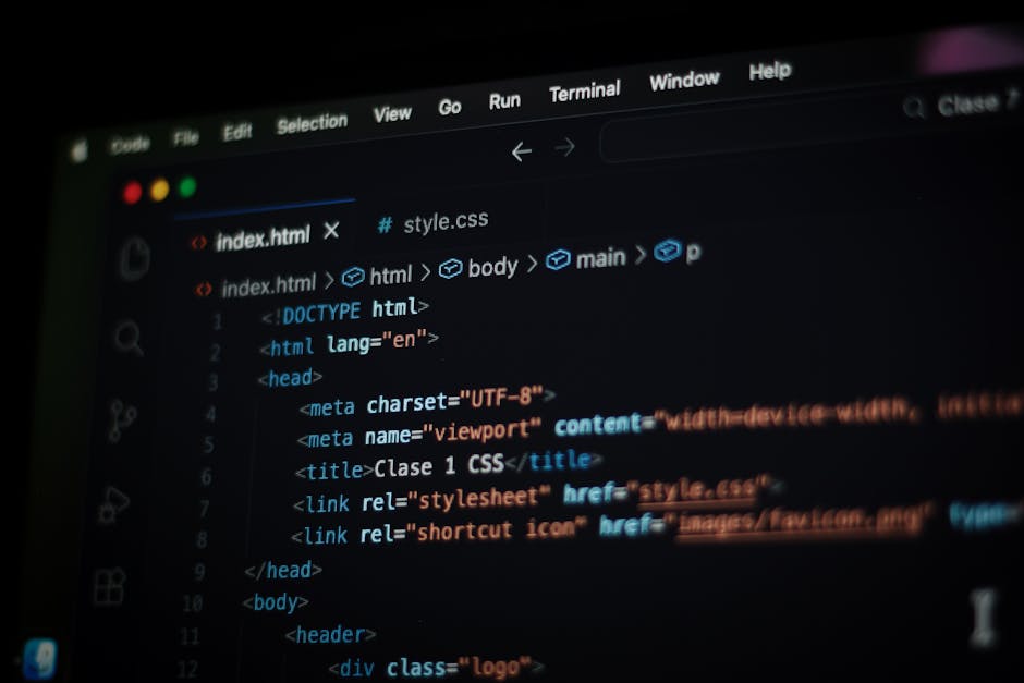 A close-up view of a person's hand using a laptop placed on a wooden desk, with the screen displaying lines of colorful programming code. The individual is wearing a dark wristwatch, and the focus is 